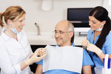 21246880 - dentist explaining teeth model to male patient at clinic